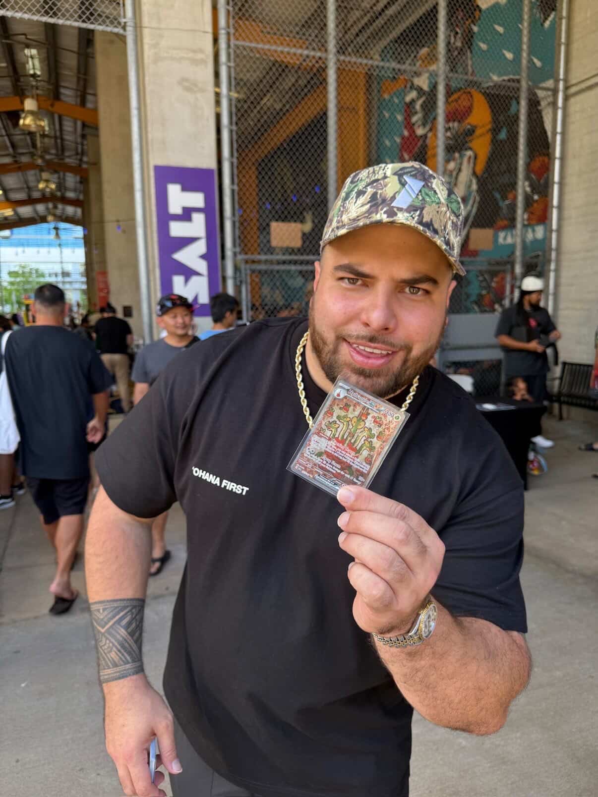 Attendee in OHANA FIRST tee holding up a Pokemon card pull at the SALT Kaka'ako entrance